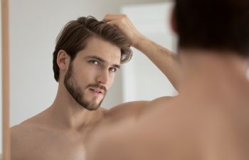 Attractive middle-aged man looking in a mirror and combing his hair with his fingers.